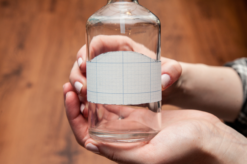 Woman holding a label prototype around a glass bottle.