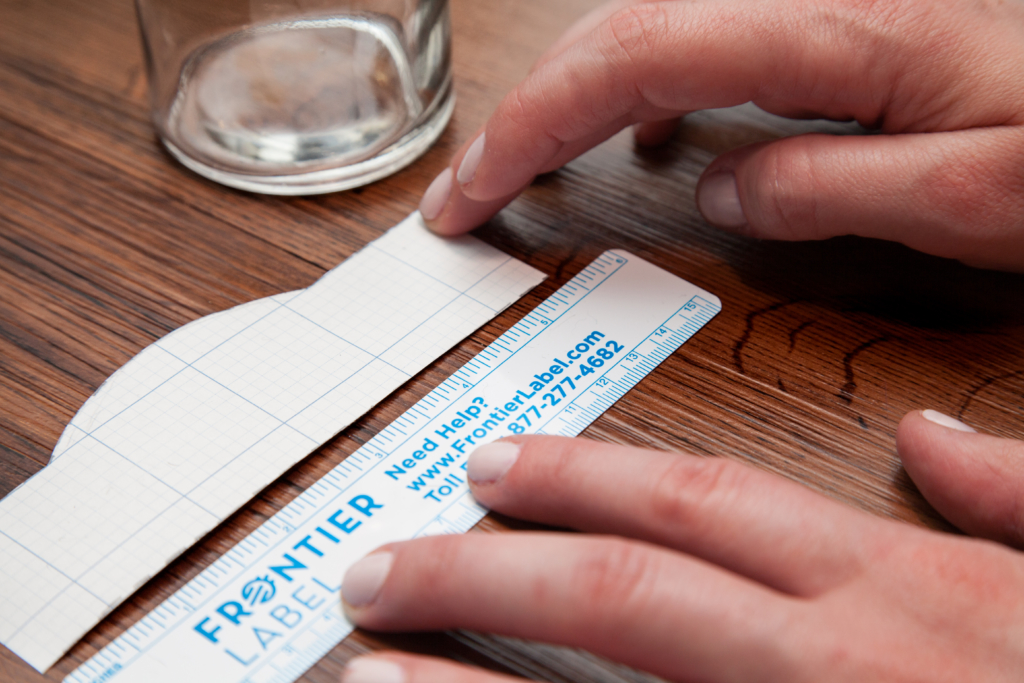 Woman measuring the length of a label prototype with a ruler.