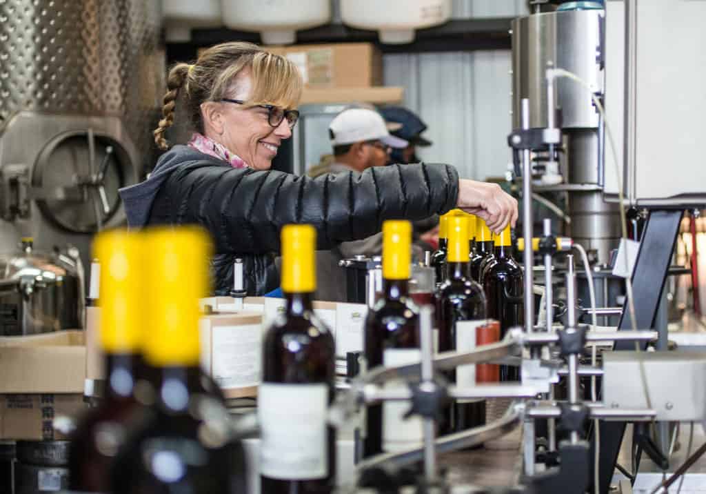 Woman smiling as she labels bottles of wine.
