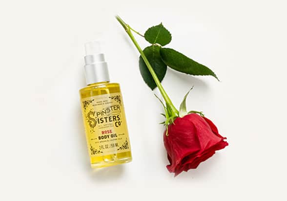 Spinster Sisters Rose Body Oil laying next to a red rose.