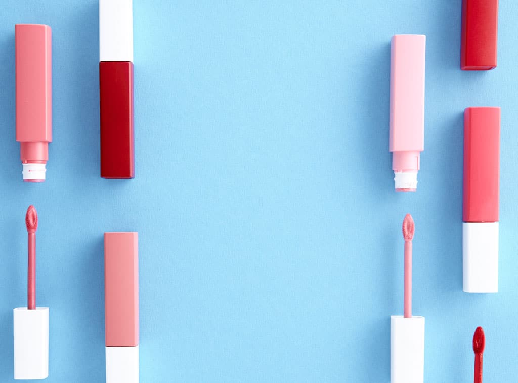 An assortment of pink lip gloss tubes on a bright blue background.