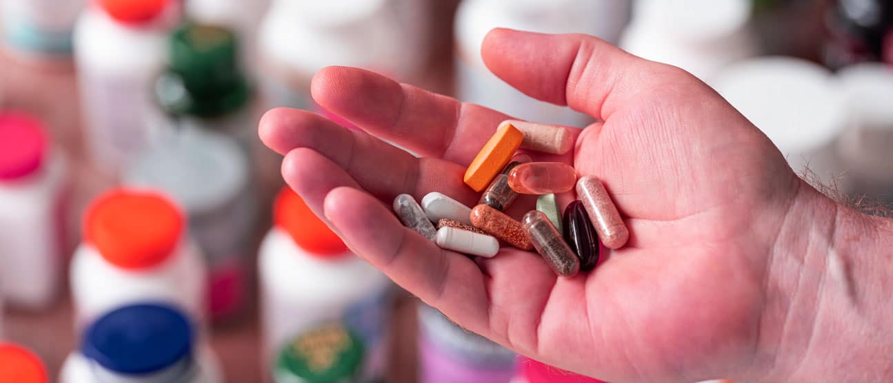 Man holding a handful of supplements with vitamin bottles in the background.