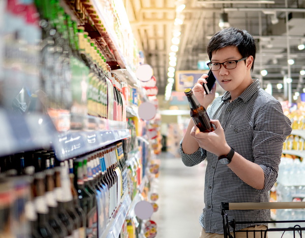 man reading beer bottle label in a grocery store