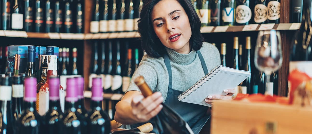 Young woman looking at a wine bottle while working in a wine shop.